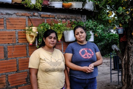 Dos mujeres están de pie junto a una pared con cestas colgantes de flores.