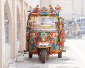 A brightly decorated orange tuk at the side of a road
