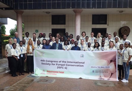 A group of African and European people all wearing lanyards and holding a banner outside a building