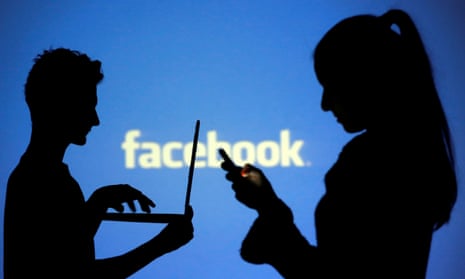Two people using personal computers in front of a Facebook logo