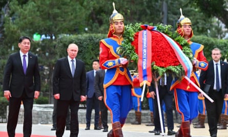 Putin and Khürelsükh walk along a red carpet behind soldiers in blue and red uniforms with gold headpieces