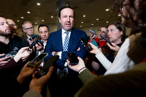 スーツを着た男性が、自分の方に向けて携帯電話を構えている人々のグループに話しかけている。