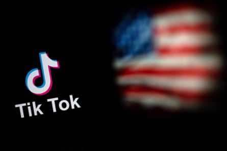 Um logotipo do TikTok é mostrado em um smartphone com uma imagem borrada da bandeira americana ao fundo.