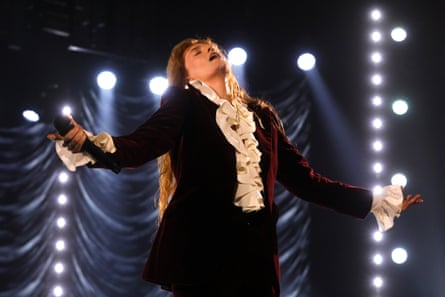 In dark velvet blazer and frilly white shirt, Florence Welch throws her head back with her eyes closed, clasping her microphone in her right hand
