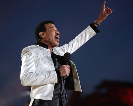 A photograph of Lionel Richie performing on stage, one hand pointing up and the other holding a microphone.