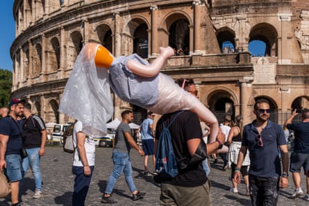 Visitors walk past the Colosseum carrying inflatable souvenirs during peak tourist season