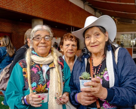 Two smiling older women hold small potted succulents, one wearing a wide white hat