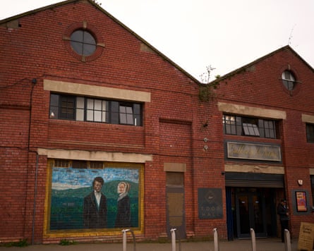 The exterior of a brick former factory with a mural of a Victorian man and woman on the wall.