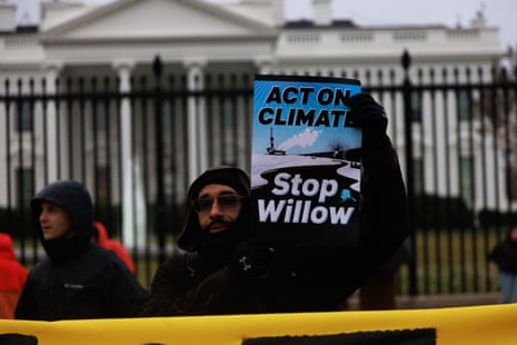 A man holds a 'Stop Willow' sign in front of the gates to the White House.
