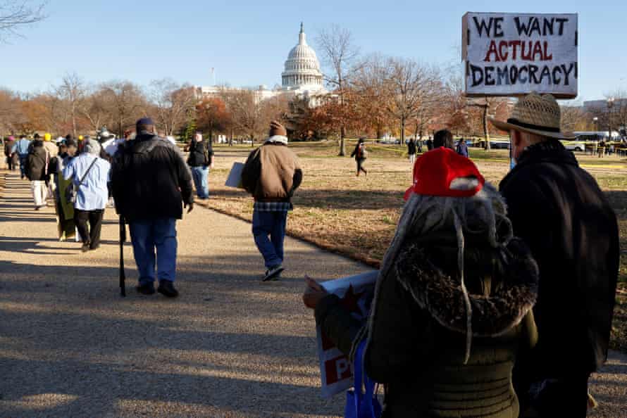 People walk towards the US Capitol, one of them holding a sign that says, "We want actual democracy!"