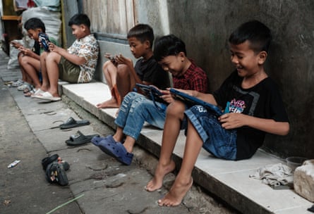 Bambini seduti a terra a guardare smartphone e tablet in un vicolo