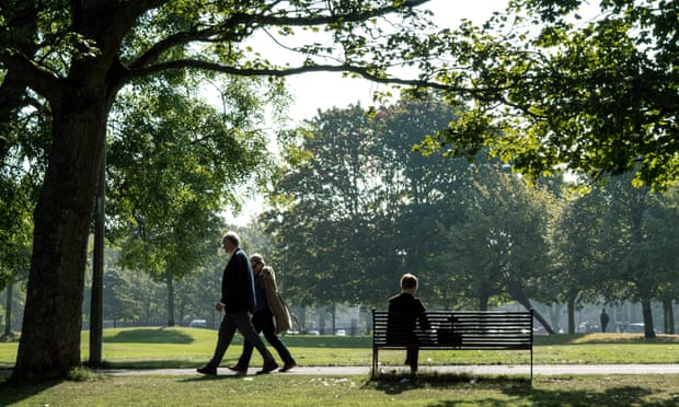 Man sat on bench with two people walking past in Bruntsfield Links Park, Edinburgh.