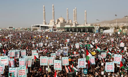Endless crowds of people holding white, red and green signs, with building with six minarets in the background.