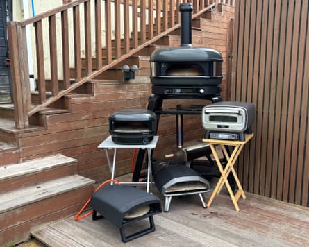 Five pizza ovens arranged on wooden decking outdoors.