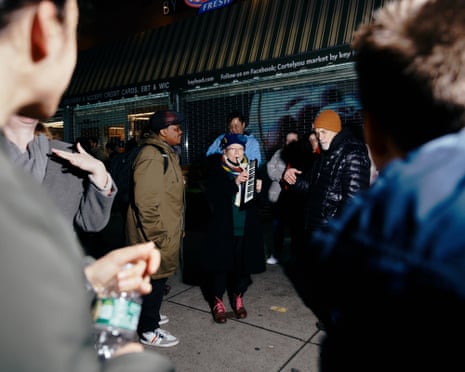 Woman in cap and jacket plays an instrument while people look on.