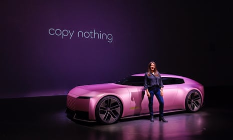 The Jaguar Type 00 in Miami pink with the slogan 'copy nothing' in the background and a woman standing beside the car.
