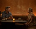 Two actors sit in a darkened bar at a circular table with a candle in a glass holder on it in a still from the comedy series Colin from Accounts