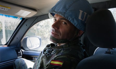 Lt Col José Irisarri, wearing a helmet, looks towards the camera while travelling in a vehicle