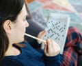 A young woman with dark hair and a fair complexion holding a pencil and solving a crossword puzzle