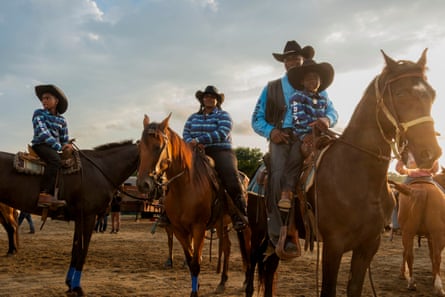 A man with three young children in cowboy hats sit atop horses