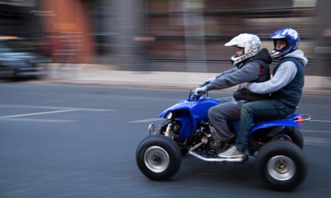 Two people wearing helmets on a quad bike on the road