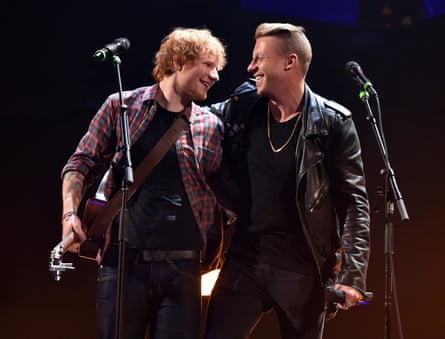 Man with red hair and a checked shirt next to man with quiff dressed in black leather jacket, both in front of microphones