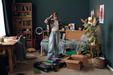 Teenager girl standing in messy bedroom with a suitcase and cardboard boxes