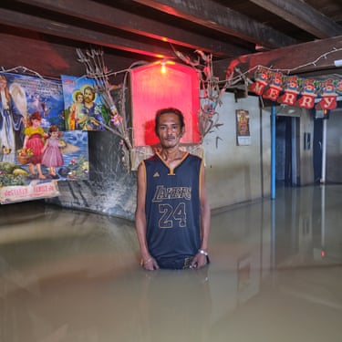 A man stands in a room thigh-deep in flood water with colourful pictures in the background