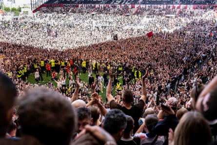 St Pauli players celebrate on the pitch surrounded by thousands of supporters after confirming promotion to the Bundesliga.