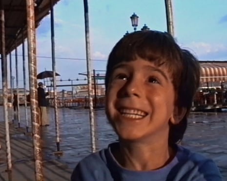 A boy grins endearingly, on a Venetian boardwalk by the water