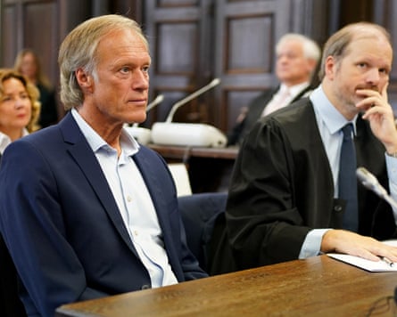 Gerhard Delling sits next to his lawyer in court; he is in his mid-60s and has greying blond hair swept back from his face; he wears a dark blue jacket with white shirt.
