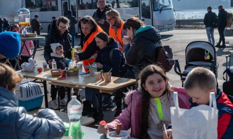 Children eat at tables in the open with prams and carriers for pets lying around them