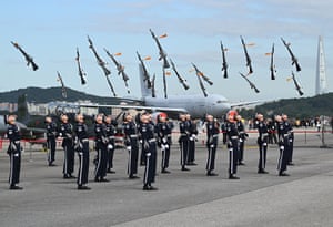 Honour guards throw their rifles in the air in front of a plane on a runway