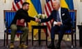 Volodymyr Zelenskiy shakes hands with Joe Biden behind their countries flags