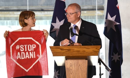 A Stop Adani protester takes to the stage where Scott Morrison was making a speech in Brisbane on Monday