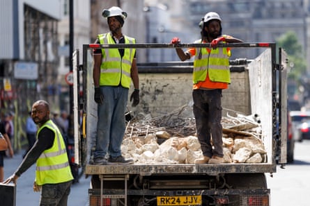 Two men in helmets and hi-vis standing on a lorry bed with rubble in it, and another worker standing next to them