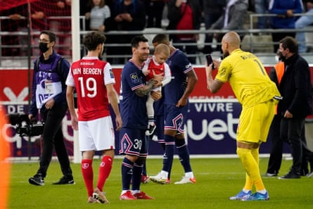 Reims goalkeeper Predrag Rajković asks Lionel Messi to hold his child for a photo.