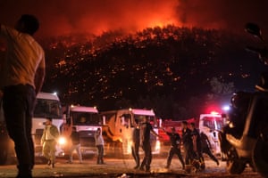 Residents and firefighters attempt to extinguish a wildfire as smoke and flames rise from a forested area