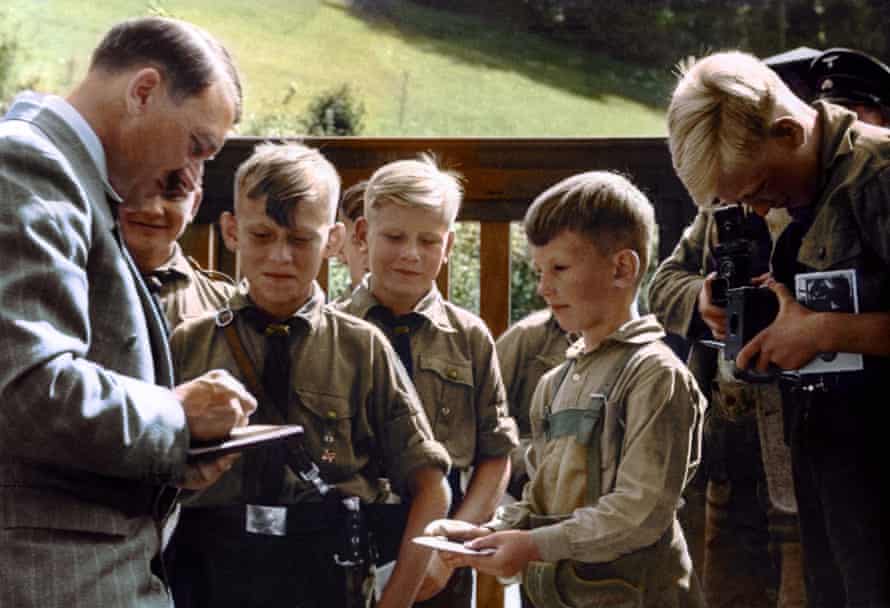 An undated photograph of members of the Hitler Youth surrounding their leader at the Berghof, his holiday retreat in the Bavarian Alps: black and white image coloured by artist Marina Amaral