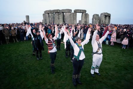 A troupe of dancers line up while a crowd watch with Stonehenge in the background