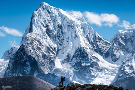 Small figure with baby on back in front of huge mountain crag