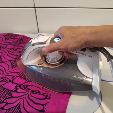 The reviewer Caramel Quin testing the Breville DiamondXpress. The iron is pressing a pink and black fabric against a white tiled wall.