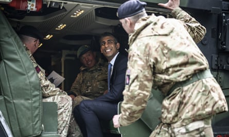 Rishi Sunak smiling broadly in a helicopter surrounded by men in combat gear