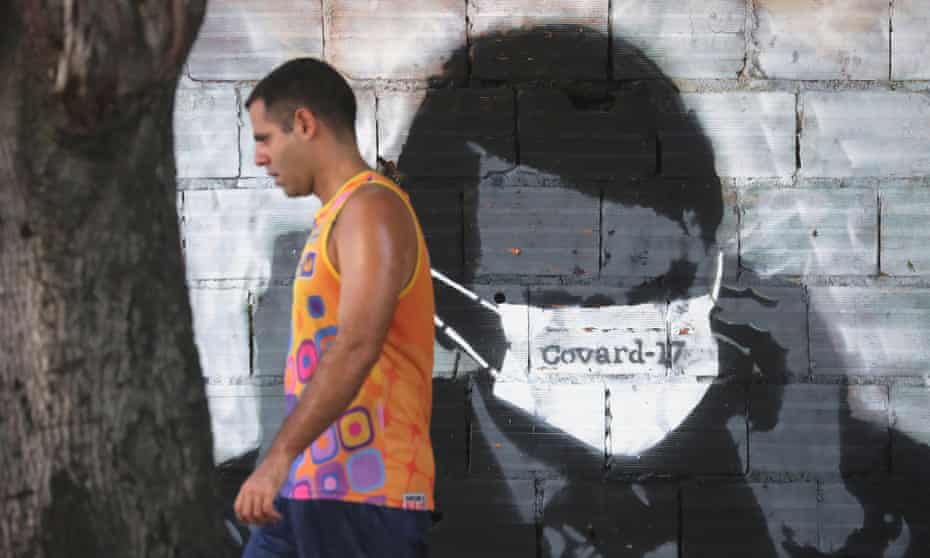 A man walks past by a graffiti depicting Brazilian president Bolsonaro adjusting his protective face mask – marked ‘Coward-17’ in Portuguese during the Covid-19 outbreak, in Rio de Janeiro. The number 17 is a reference to the number Bolsonaro used in his 2018 election campaign. Photograph: Sergio Moraes/Reuters