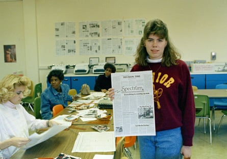 A high school student holds up a newspaper in a classroom