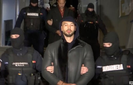 Andrew Tate, dressed in a black leather jacket and a navy hoodie, is led away by police wearing balaclavas after the raid on his home in Bucharest, Romania, in December 2022.