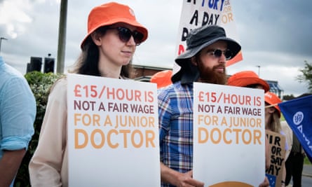 People hold signs reading: ‘£15/hour is not a fair wage for a junior doctor’