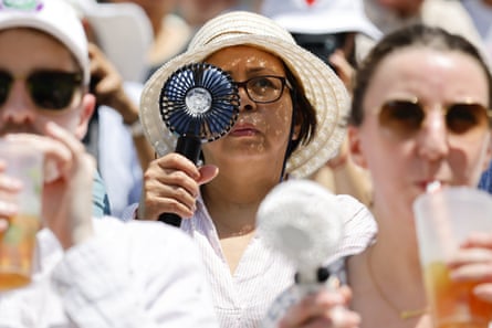 A spectator uses a fan and another drinks from a plastic cup at Wimbledon