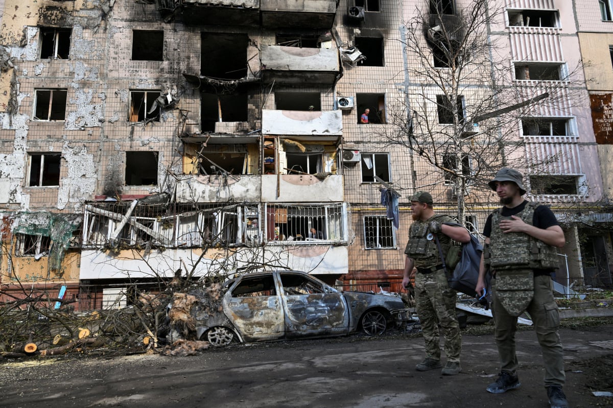 Two men in military uniform stand in front of building damaged in drone strike, in Ukraine’s Zaporizhzhia.