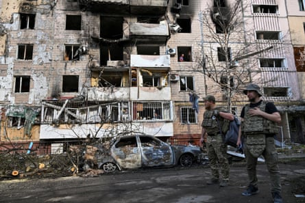 Two men in military uniform stand in front of building damaged in drone strike, in Ukraine’s Zaporizhzhia.
